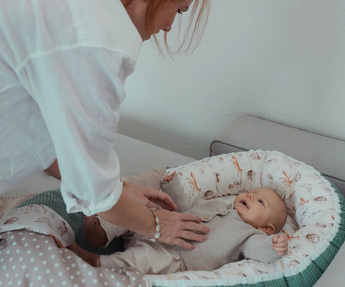 Baby im Babynest mit Mama auf dem Sofa. Babynest von ULLENBOOM im Design Waldfreunde
