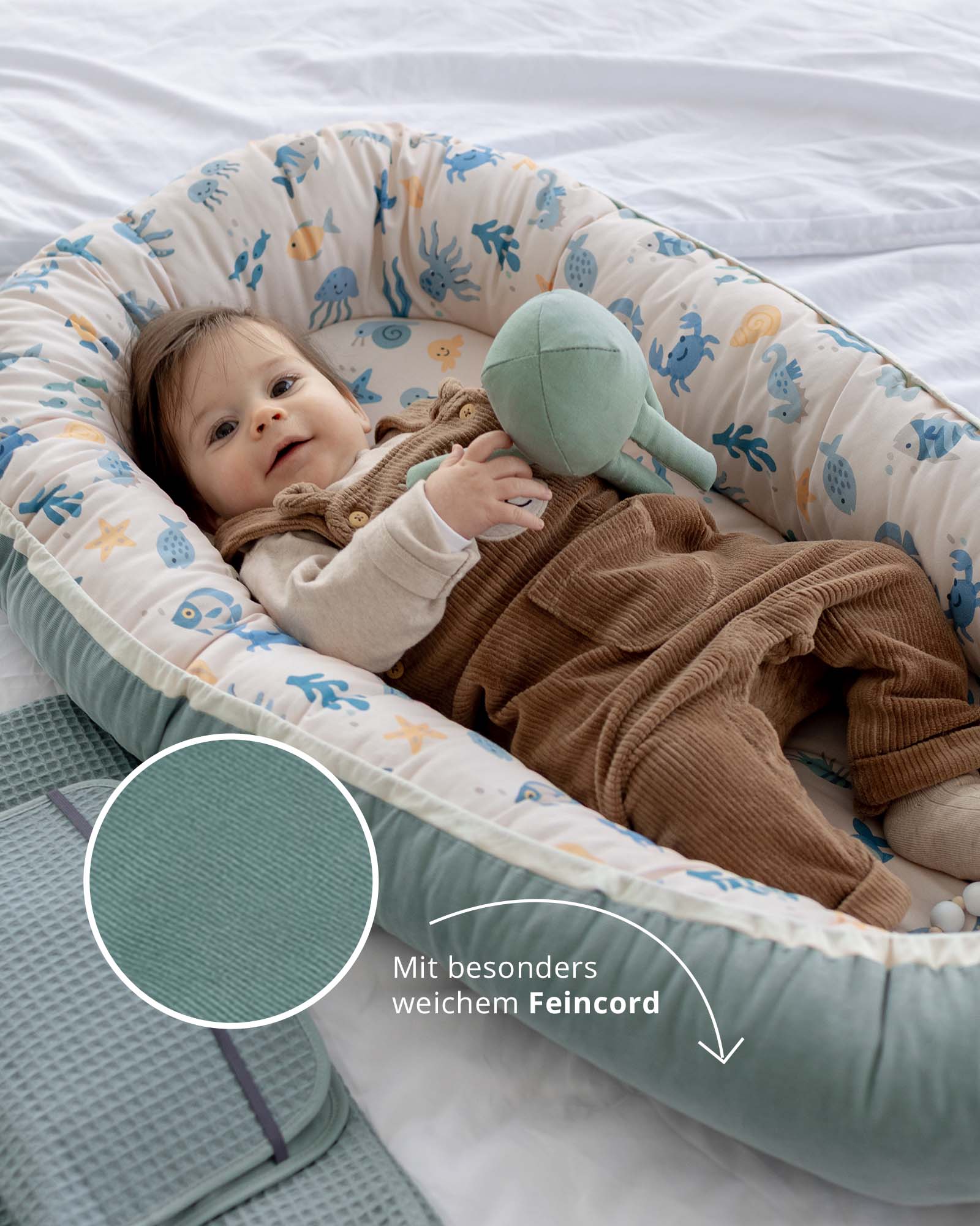 Babynest Feincord Unterwasserwelt mit Baby, das auf dem Rücken liegt und ein mintgrünes Stofftier hält.