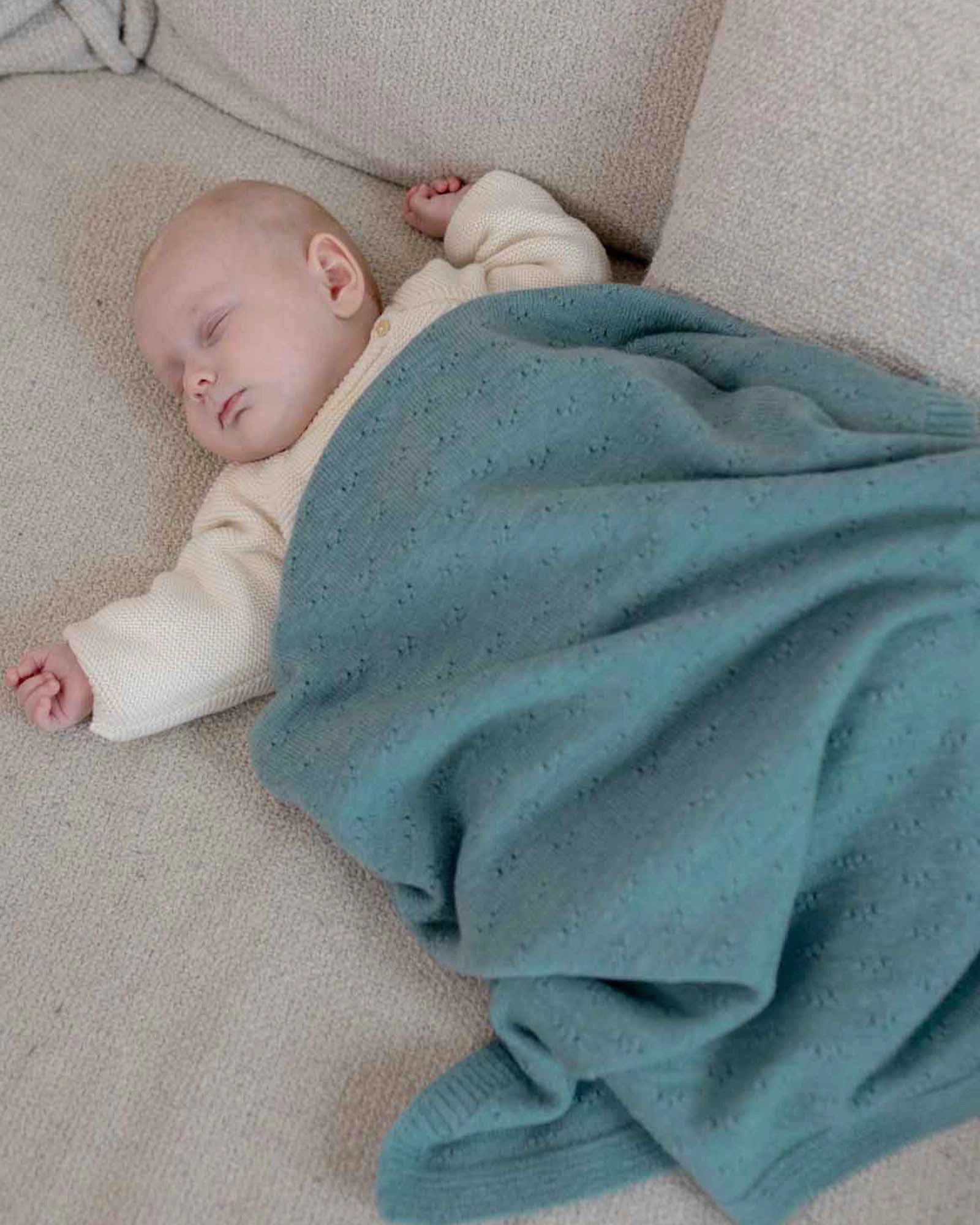 Sleeping baby covered by a soft turquoise Merino wool blanket with a subtle knit pattern.