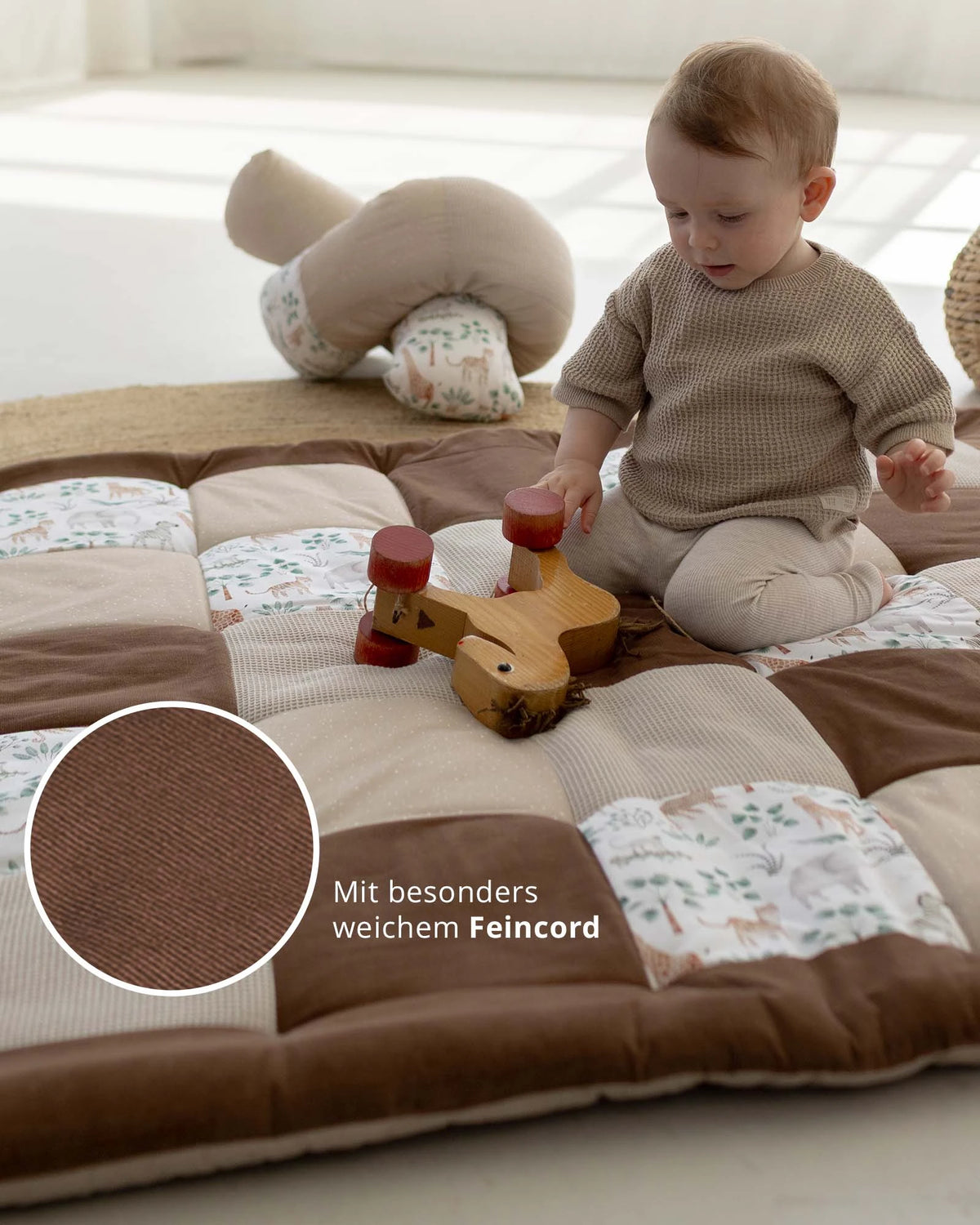 Baby spielt auf einer braunen Krabbeldecke Safari mit Patchwork-Design aus Feincord und Safari-Motiven in Erdtönen.