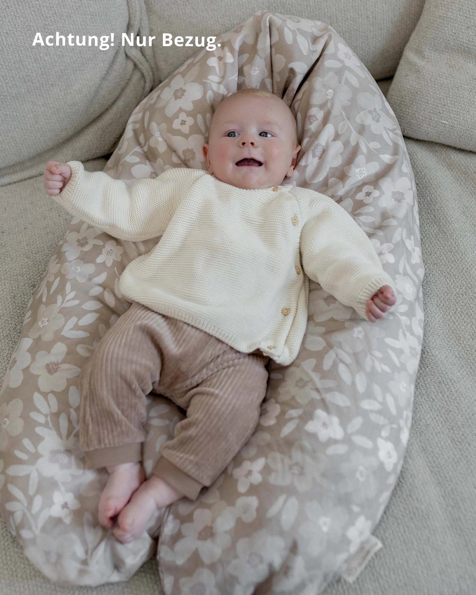 Happy baby on a beige ULLENBOOM nursing pillow cover with white floral pattern.
