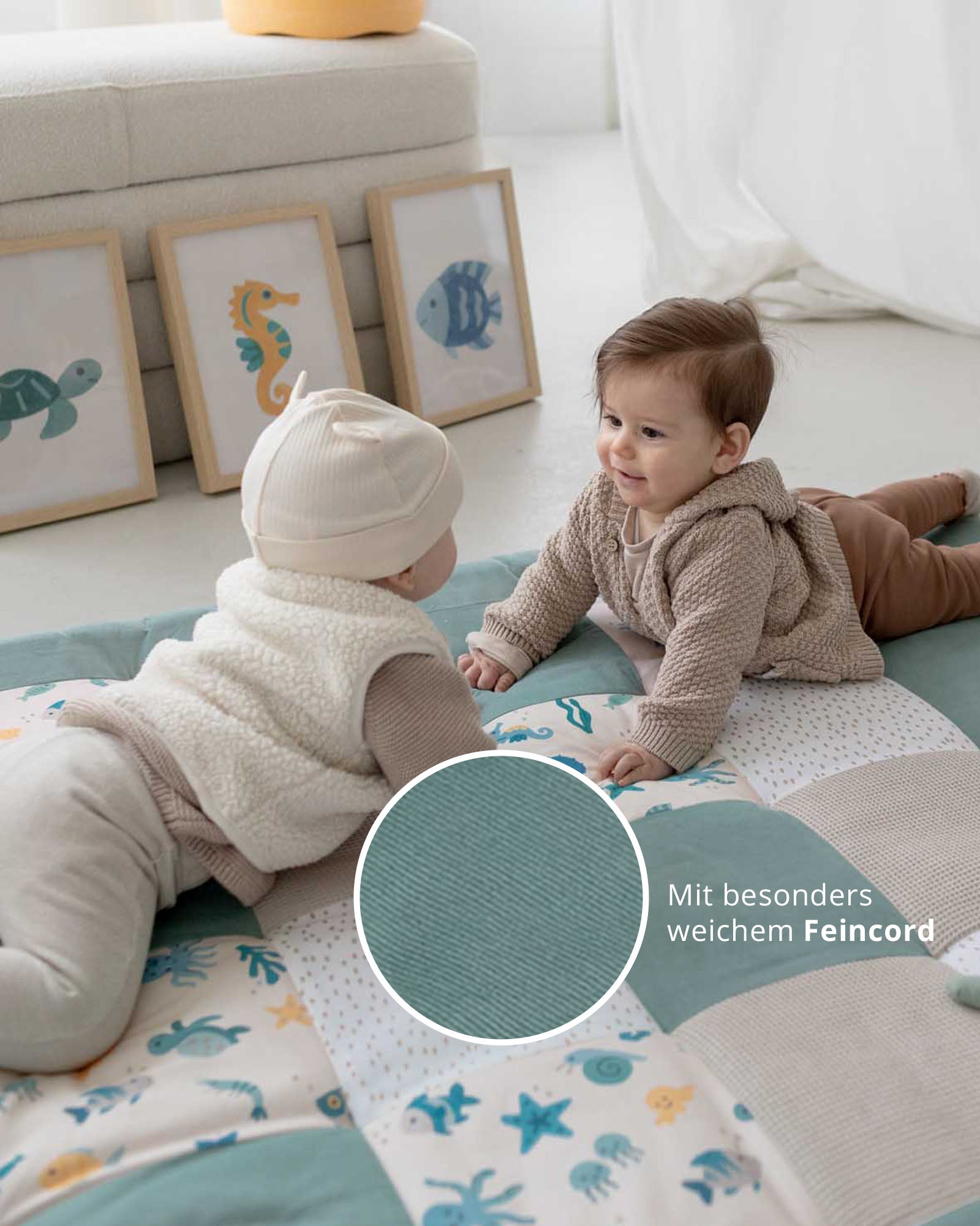 Zwei Babys spielen auf einer Krabbeldecke mit Unterwasserwelt-Motiven und Feincord-Patches in Grün- und Beigetönen.