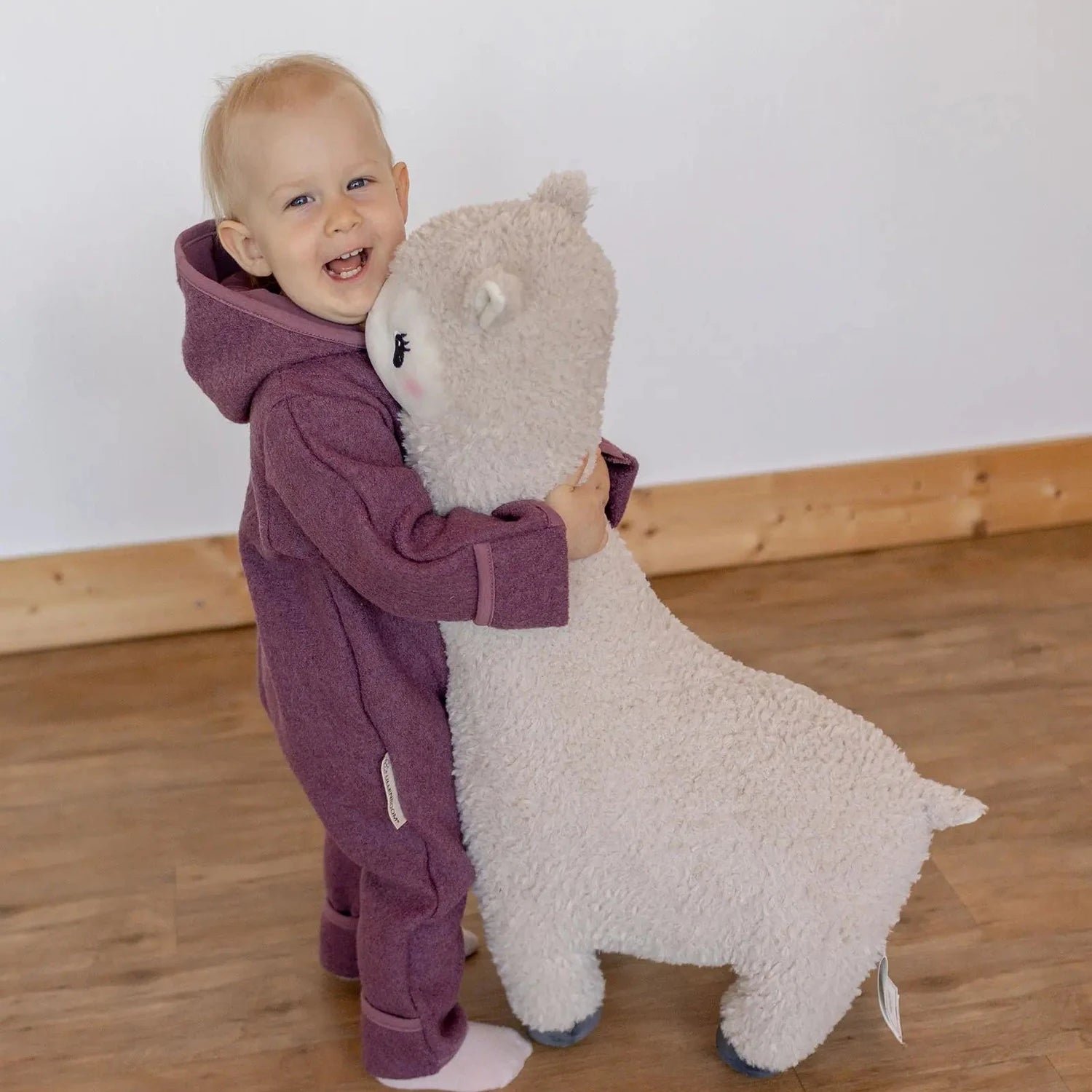 Kind im beerefarbenen ULLENBOOM Wollwalk Overall mit Kuscheltier