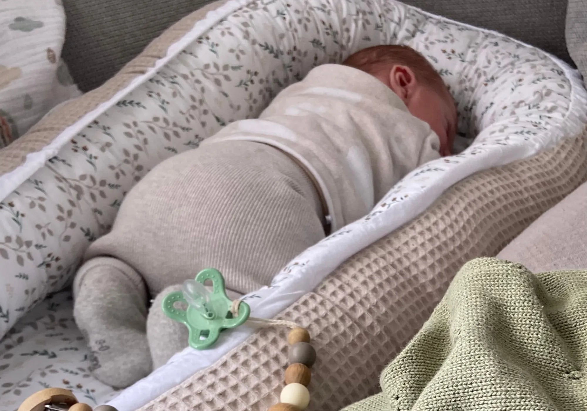 Ein Baby schläft friedlich in einem ULLENBOOM Babynest mit floralem Sandmuster und waffelgestrickter Außenseite.
