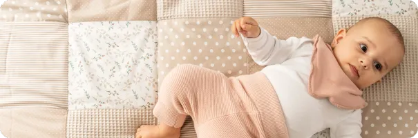 Baby liegt auf einer ULLENBOOM Sandblume Krabbeldecke mit beigen Patchwork-Mustern und floralen Akzenten.