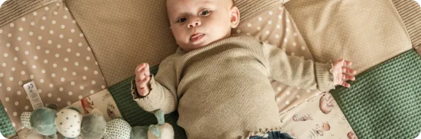 Baby liegt auf einer ULLENBOOM Waldfreunde Krabbeldecke mit beigen und grünen Patchwork-Mustern und Punkten.