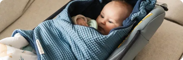 Baby in einer blauen Waffelpique Einschlagdecke mit ULLENBOOM Label, sicher in einer Babyschale liegend.