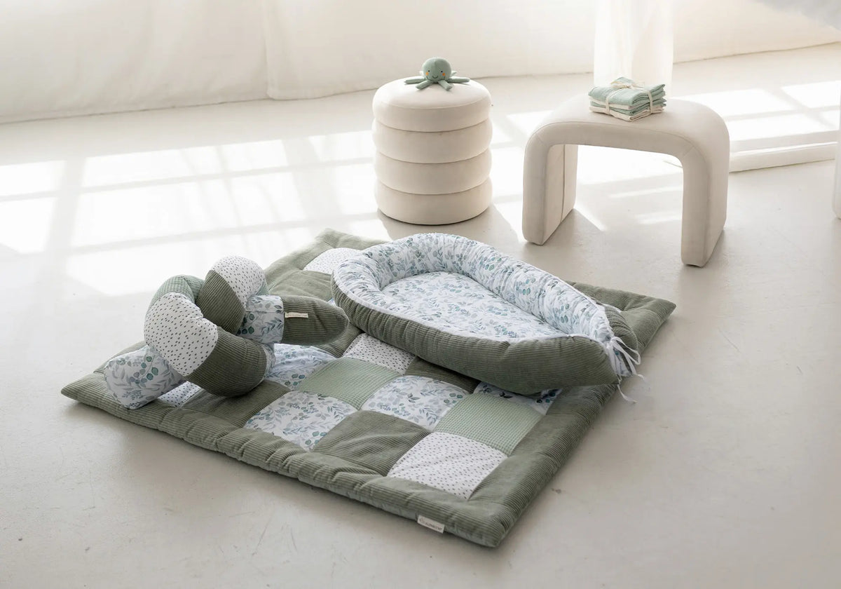 Ullenboom Babynestchen und Krabbeldecke im Patchwork-Design mit grünem Blattmuster und Cord-Stoff in einem hellen Raum.