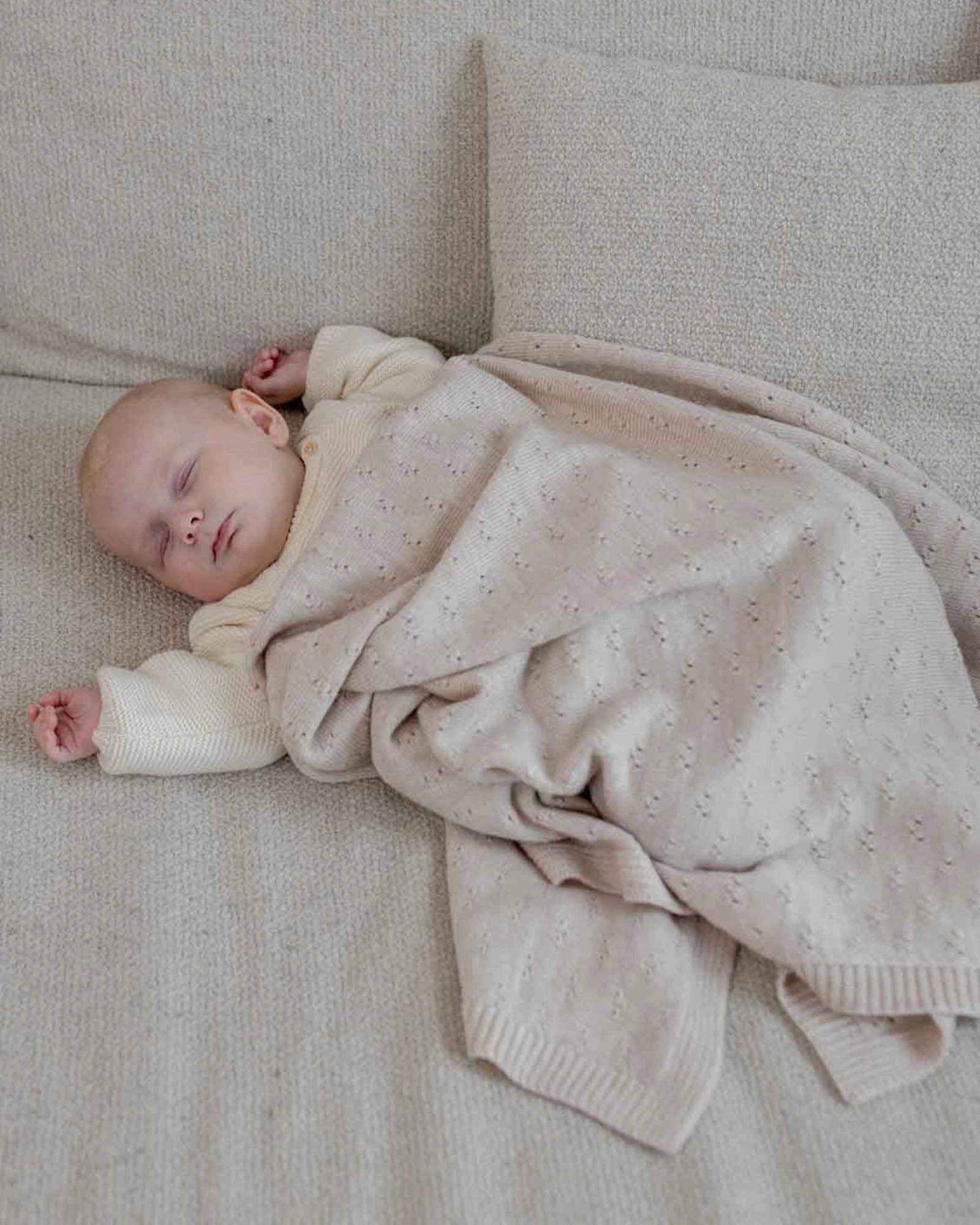 Sleeping baby covered by a soft, cream merino wool blanket with a delicate knit pattern.