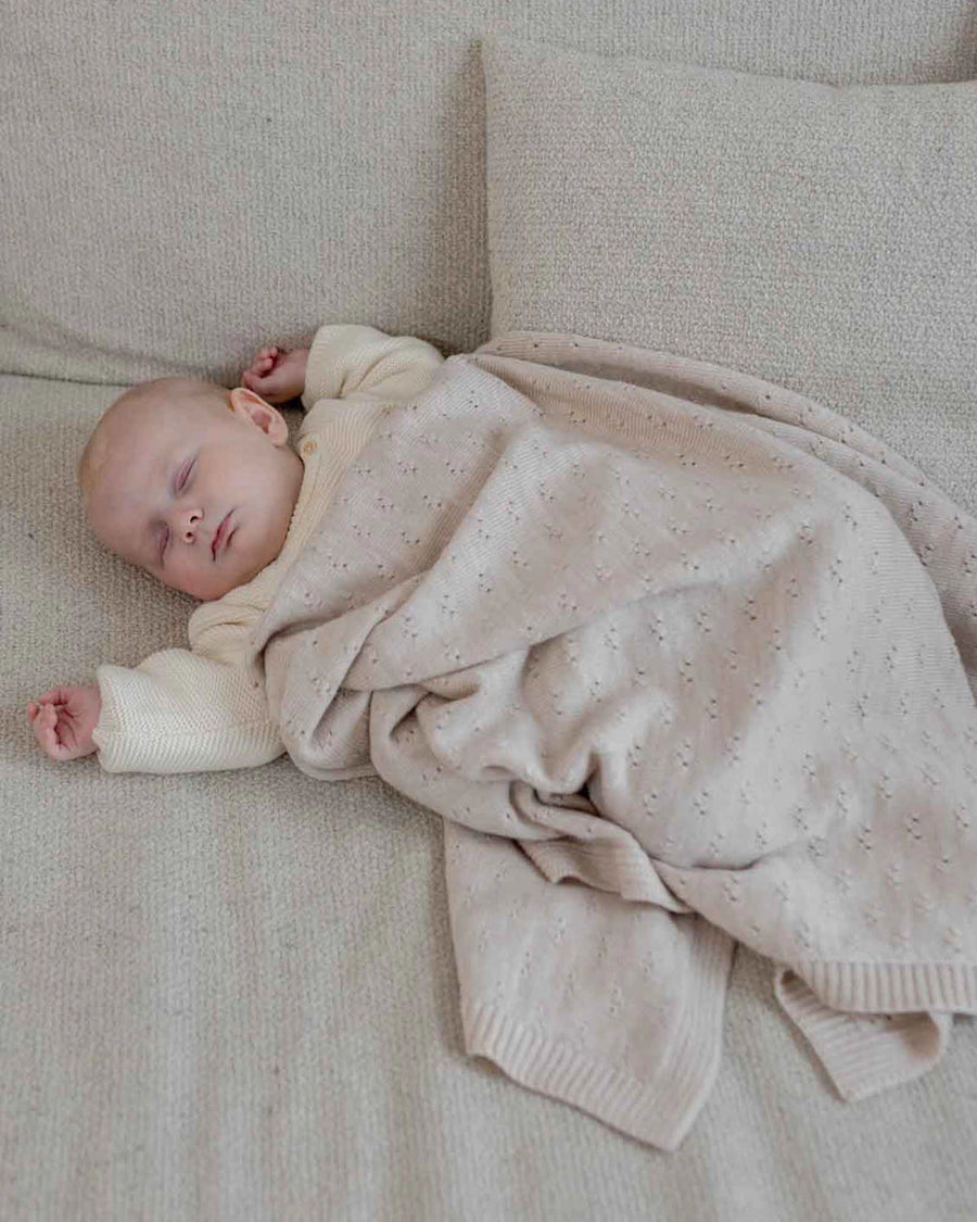Sleeping baby covered by a soft, cream merino wool blanket with a delicate knit pattern.