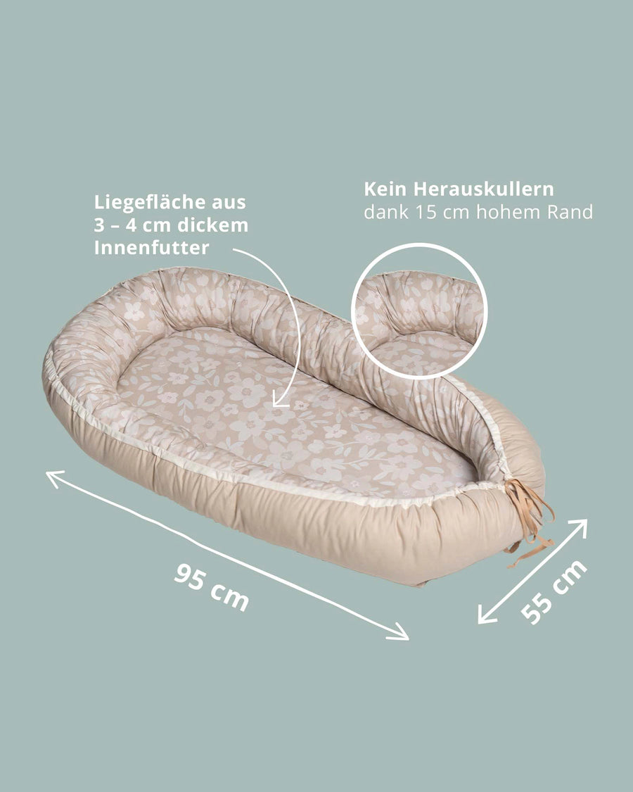 Beige babynest with floral pattern, padded sides, and adjustable ties.