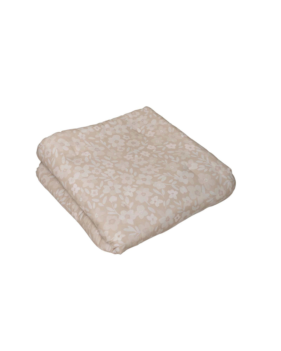 Folded beige cotton playmat with hand-painted white floral pattern.