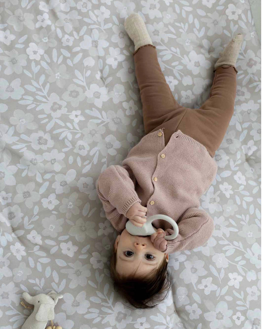 Baby on a soft, thick Krabbeldecke with hand-painted gray floral design, wearing a pink cardigan.