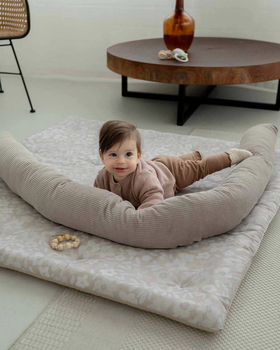Baby on a thick, soft Krabbeldecke with hand-painted floral design and a beige corduroy play nest.
