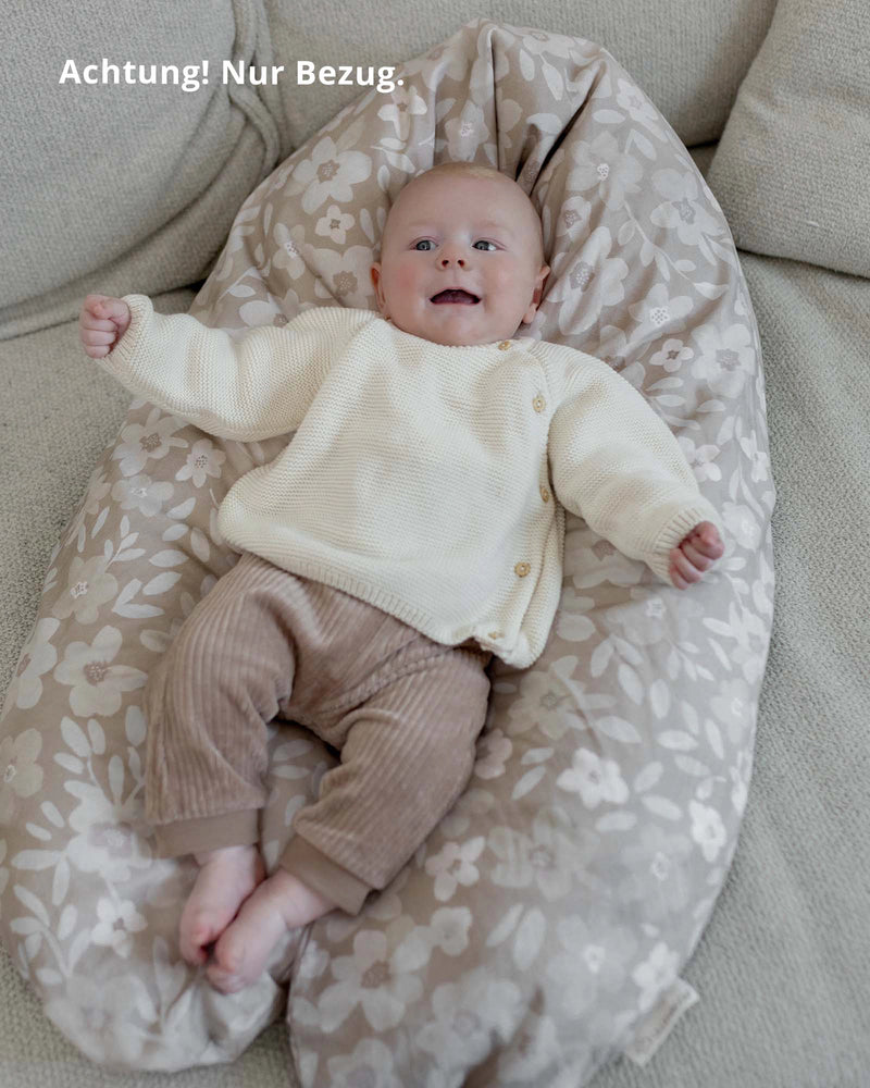 Happy baby on a beige ULLENBOOM nursing pillow cover with white floral pattern.