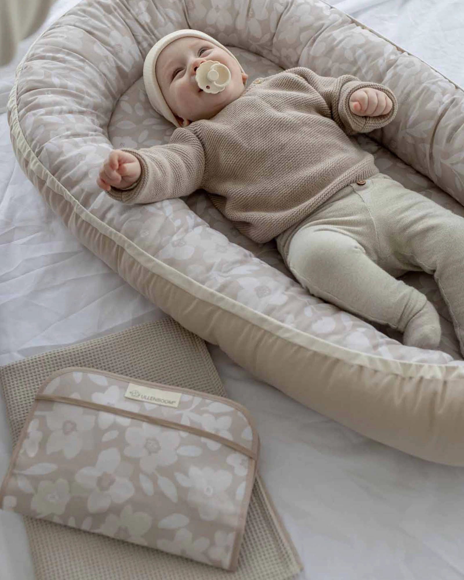 Beige baby changing clutch with floral pattern next to a baby in a matching nest.