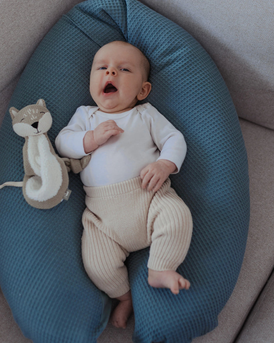 Baby liegt auf einem blauen Stillkissen mit Waffelpiqué-Bezug, daneben ein beigefarbenes Stofftier.