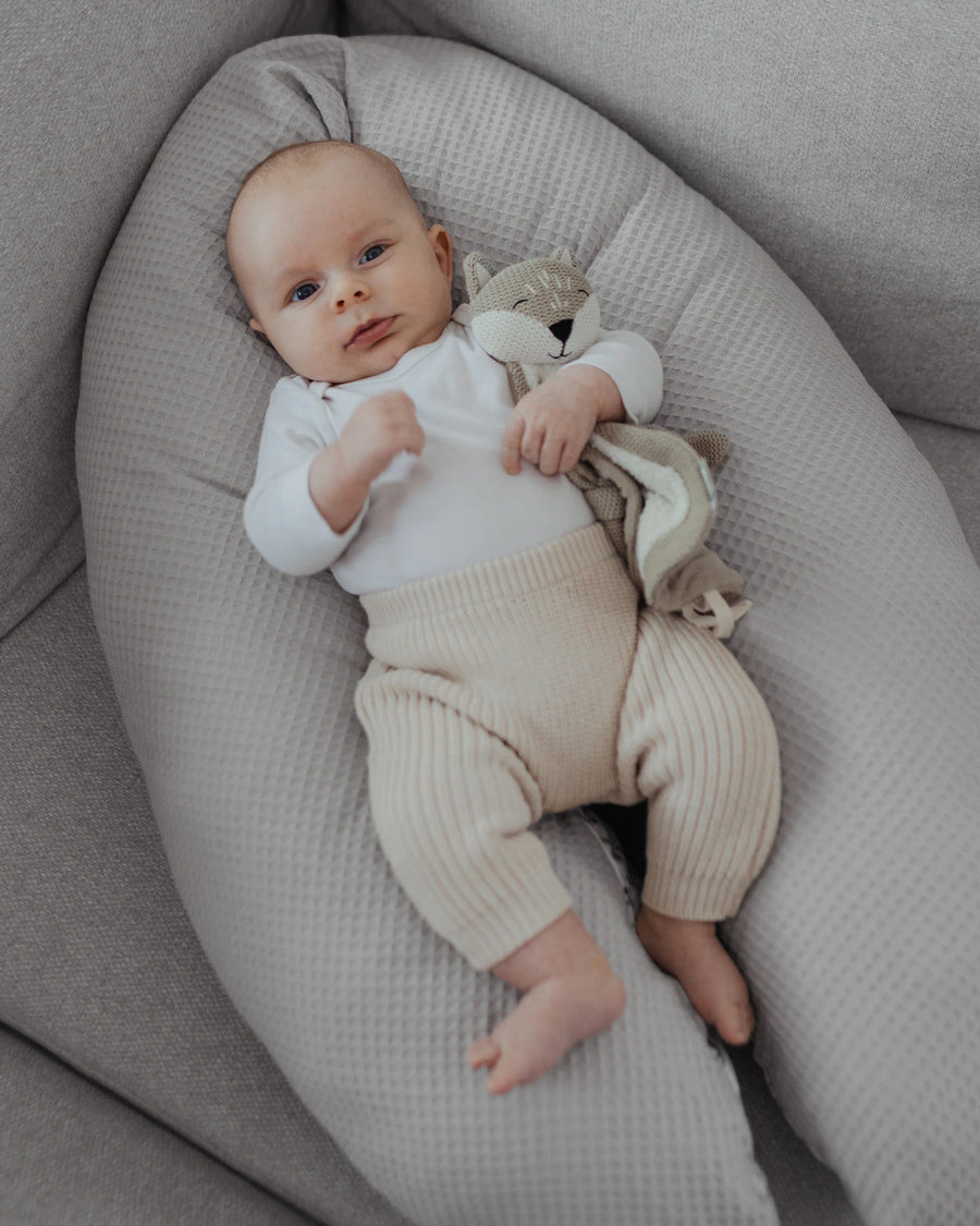 Baby liegt auf einem grauen Stillkissen mit Waffelpiqué-Bezug und hält ein kleines Stofftier in der Hand.