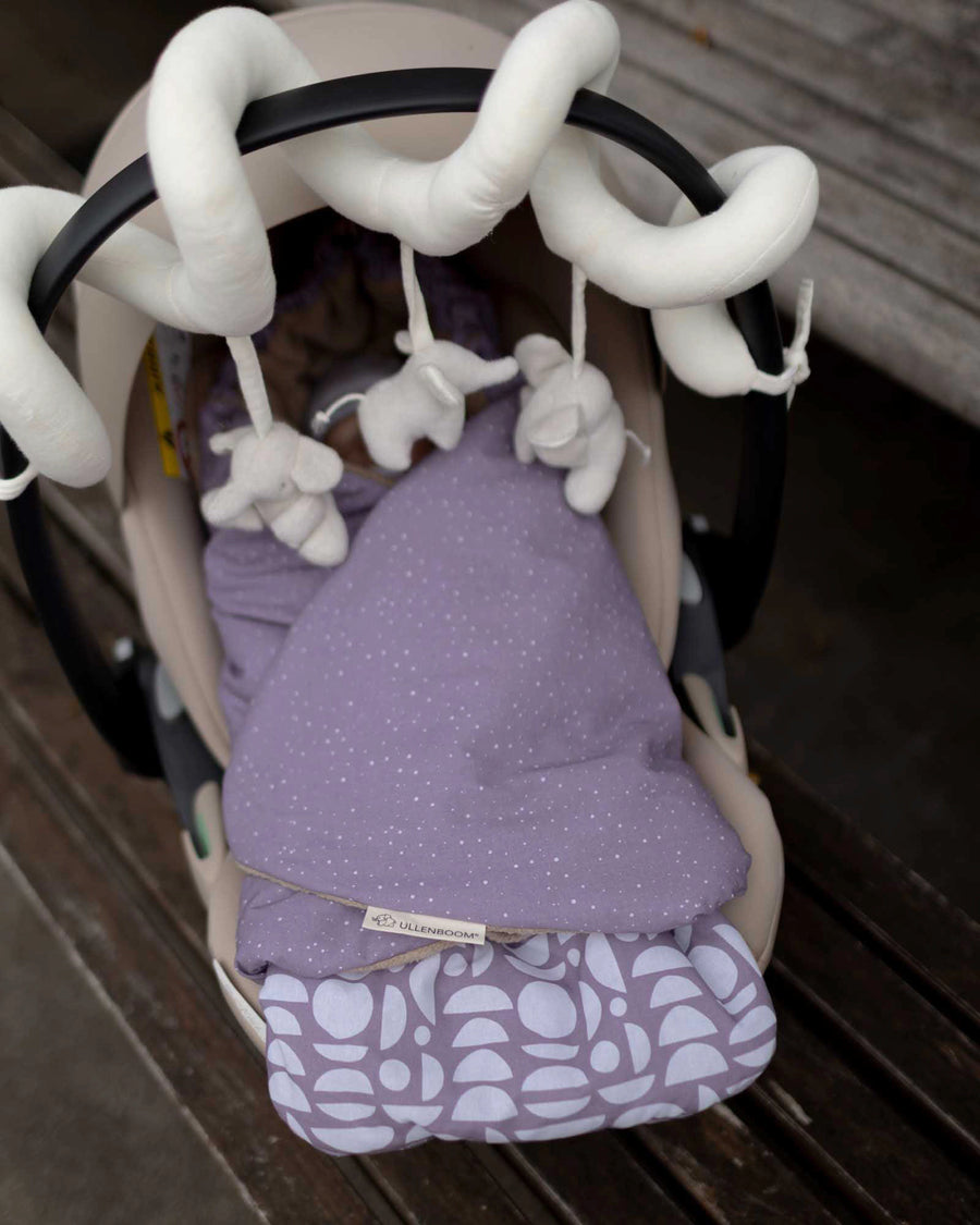 Purple ULLENBOOM baby wrap blanket with white polka dots and geometric pattern in a car seat.