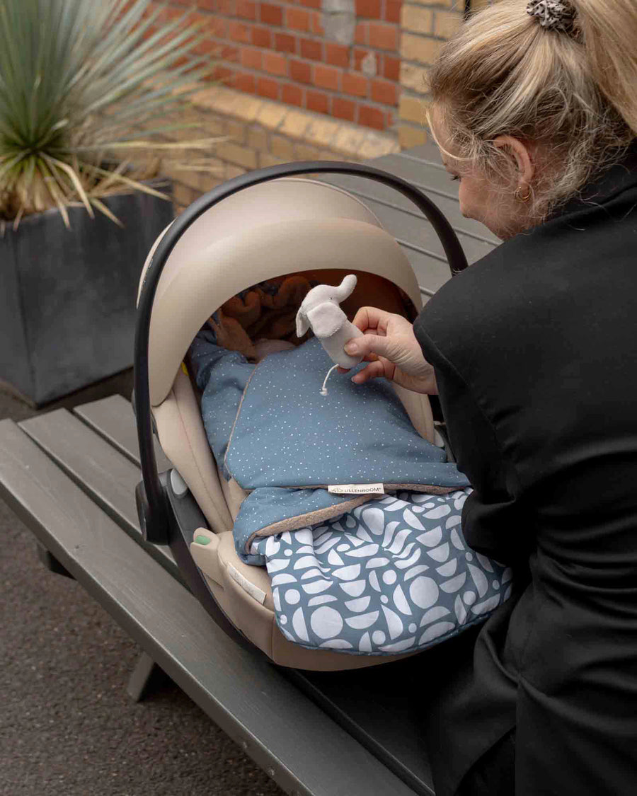 Blue Einschlagdecke Classic with white polka dots and geometric patterns, securing a baby in a car seat.