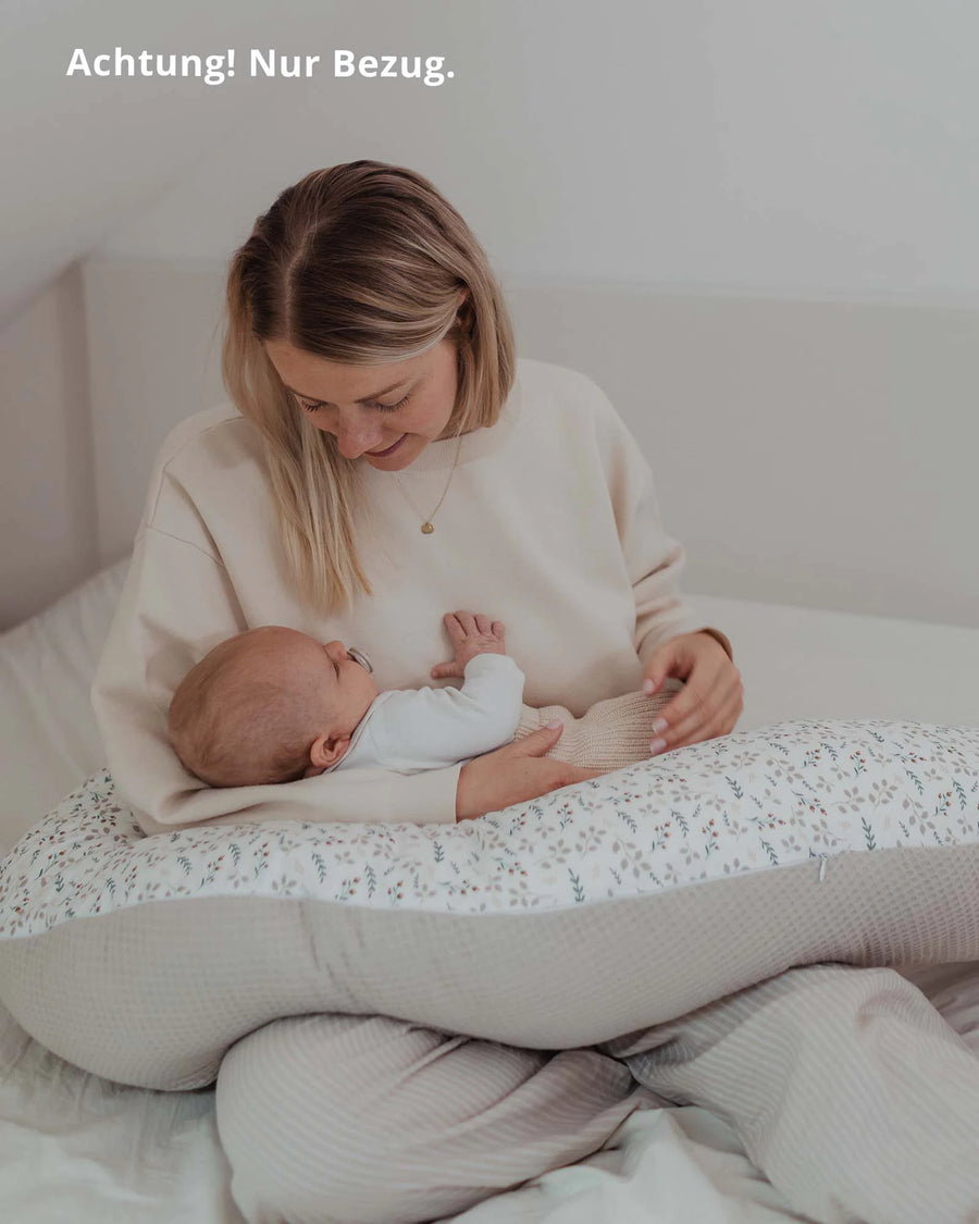 Mutter hält Baby auf einem Stillkissen mit floralem Sand-Muster und beigem Streifen-Design, aus Baumwolle.