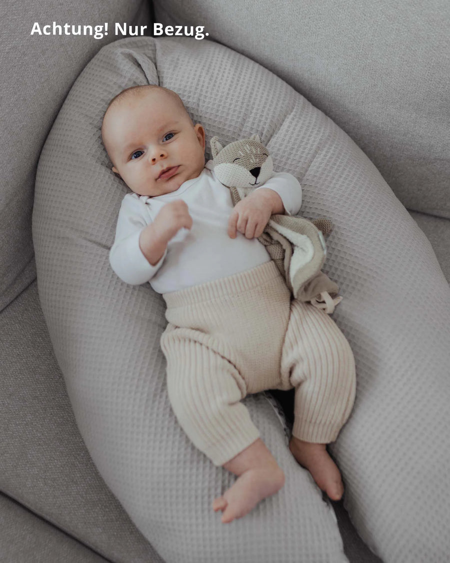 Baby liegt auf einem grauen Stillkissenbezug aus Waffelpiqué, hält ein kleines Stofftier.