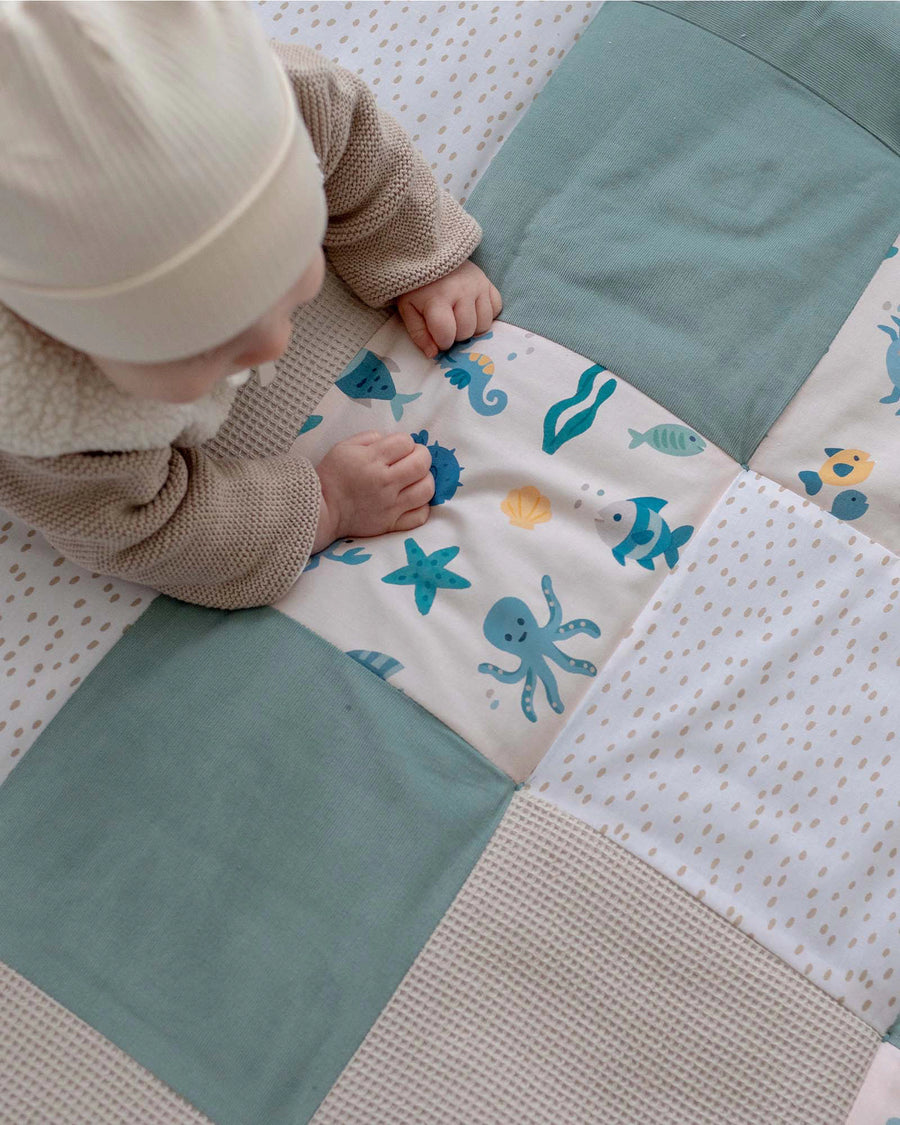 Baby on a soft, quilted play mat with blue, beige, and underwater animal squares.