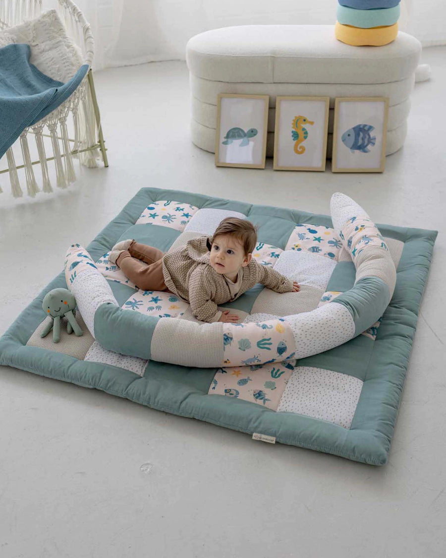 Baby on a soft, thick quilted playmat with an underwater world design and a crescent-shaped baby nest.