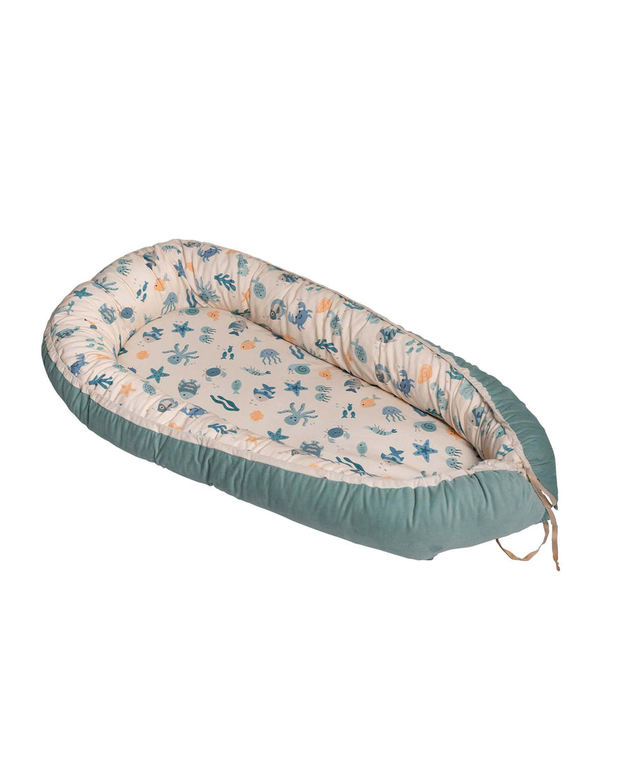 Reversible baby nest with an underwater world pattern on cream and a solid teal exterior.
