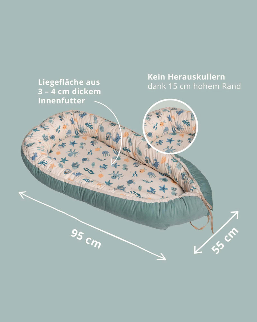 Reversible baby nest with an underwater world pattern, teal exterior, and adjustable size.