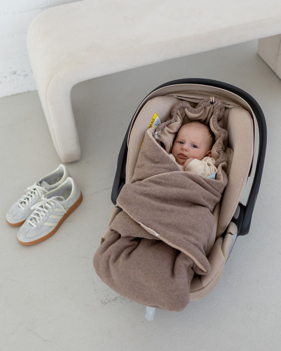 Baby in der Babyschale, eingekuschelt in die Einschlagdecke Fleece Braun