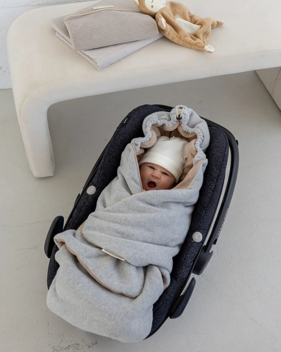 Baby in der Babyschale, eingekuschelt in die Einschlagdecke Fleece Grau