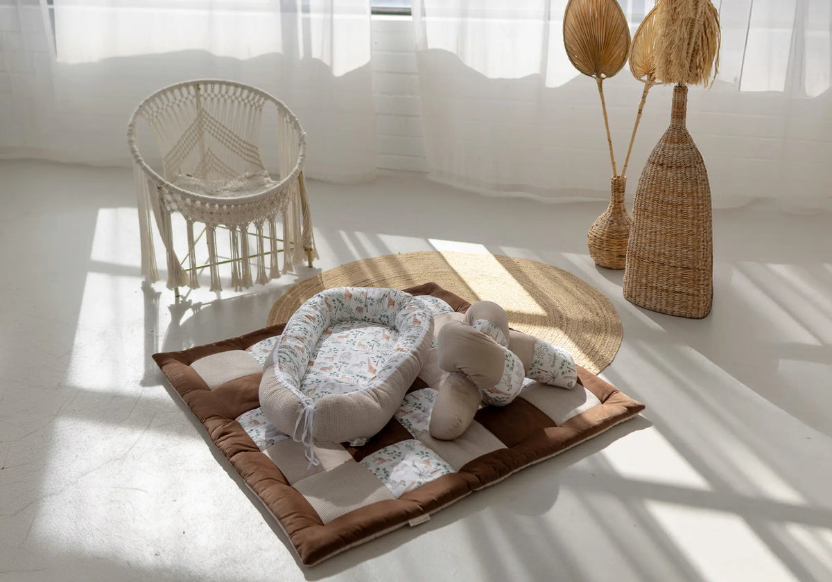 Ullenboom Babynestchen mit passendem Kissen auf einer braun-beigen Patchwork-Krabbeldecke in einem hellen, boho-inspirierten Raum.