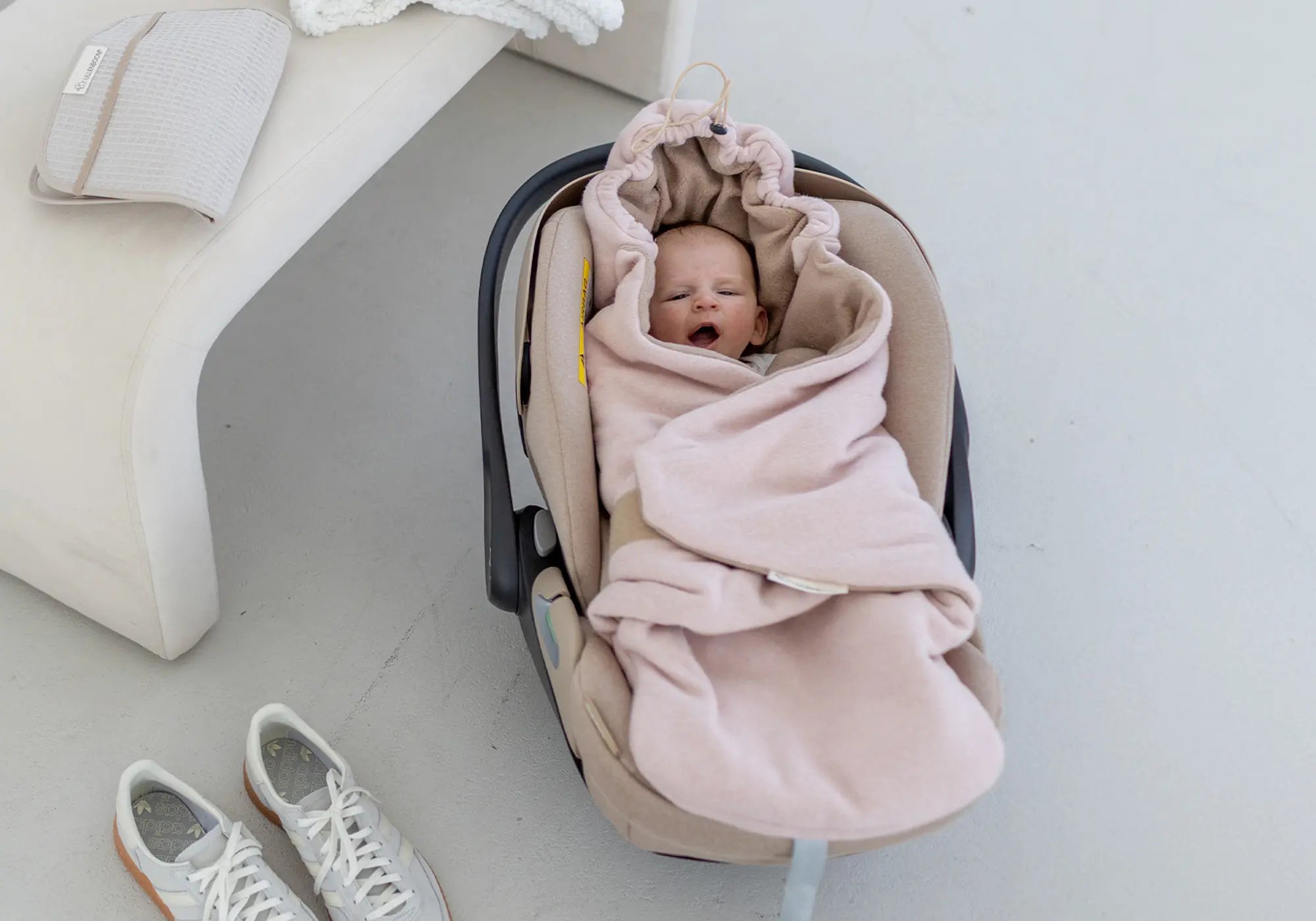 Ein Baby liegt in einer beigen Babyschale, eingewickelt in eine weiche, altrosa ULLENBOOM Einschlagdecke aus Fleece.